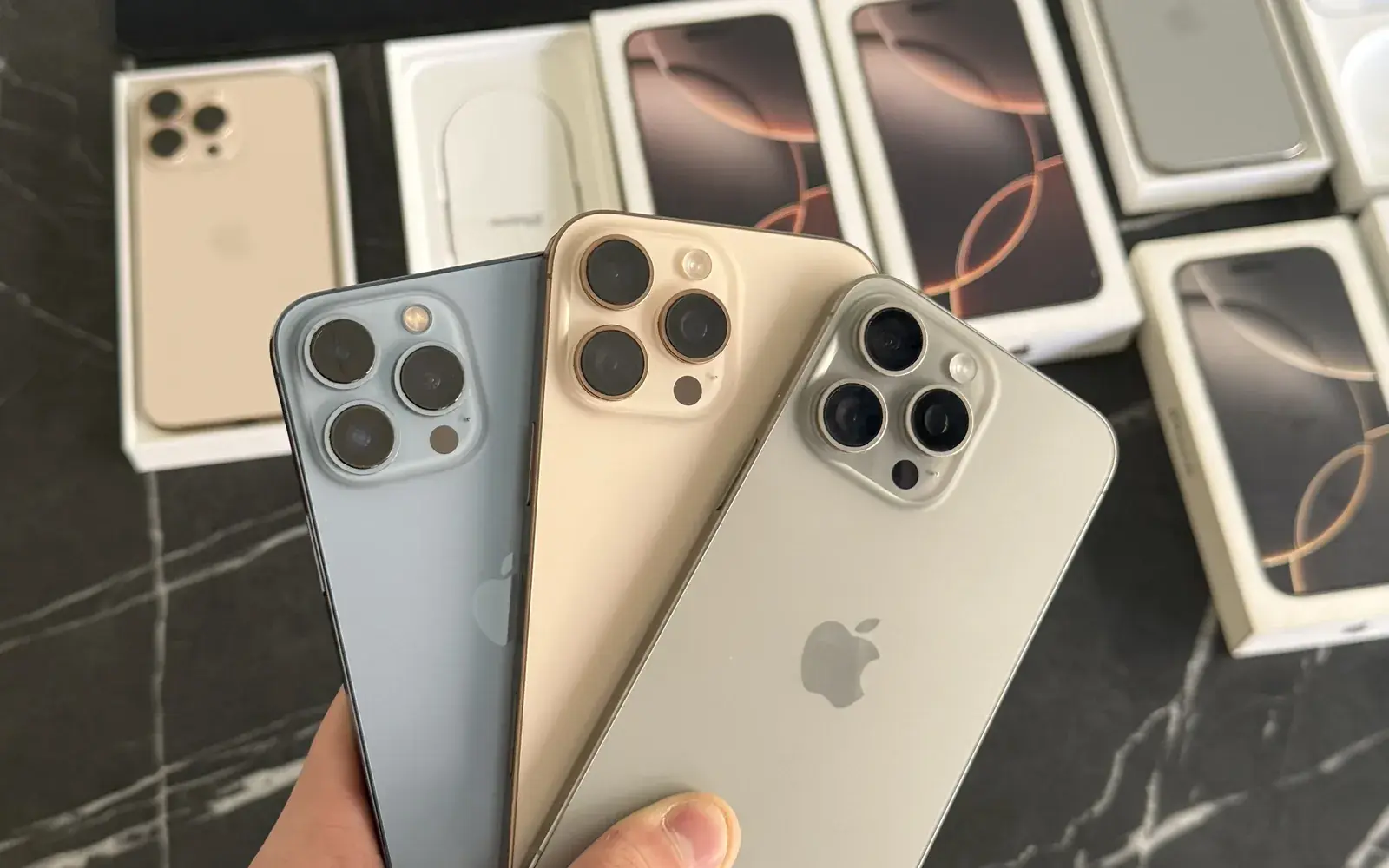 Tres iPhone Pro fuera de la caja, en la mano, con cajas de iPhone detrás